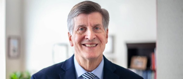 Robert Salata smiles wearing a navy suit, blue shirt, and diagonally-striped tie.