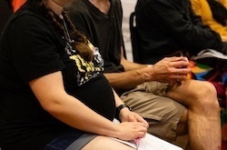 Three pregnant women stand side by side, holding their bellies.  They wear neutral or pastel-colored shirts.